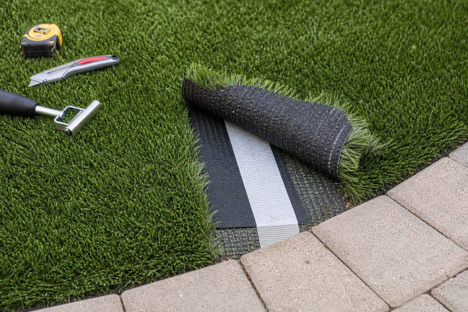 Turf backing and seam tape beside a paver edge